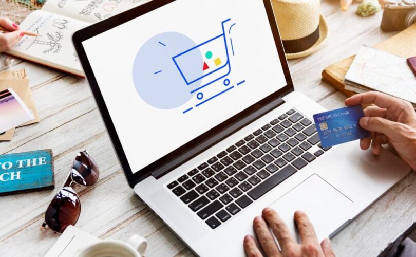 A person holding a credit card, shopping online with a laptop displaying a cart icon