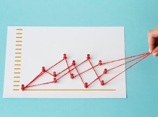 Hand pulling a string graph on paper showing a rising trend against a blue backdrop
