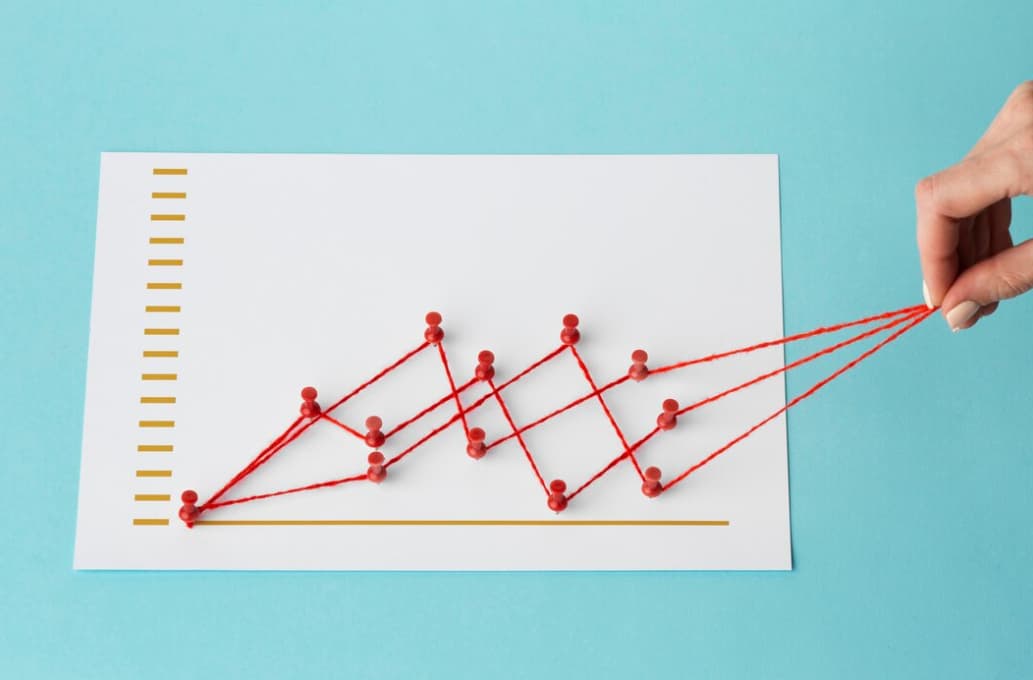 Hand pulling a string graph on paper showing a rising trend against a blue backdrop