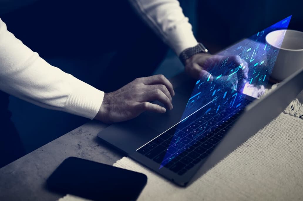 person in white sweater typing on laptop keyboard on the table, phone, and cup of coffee near it