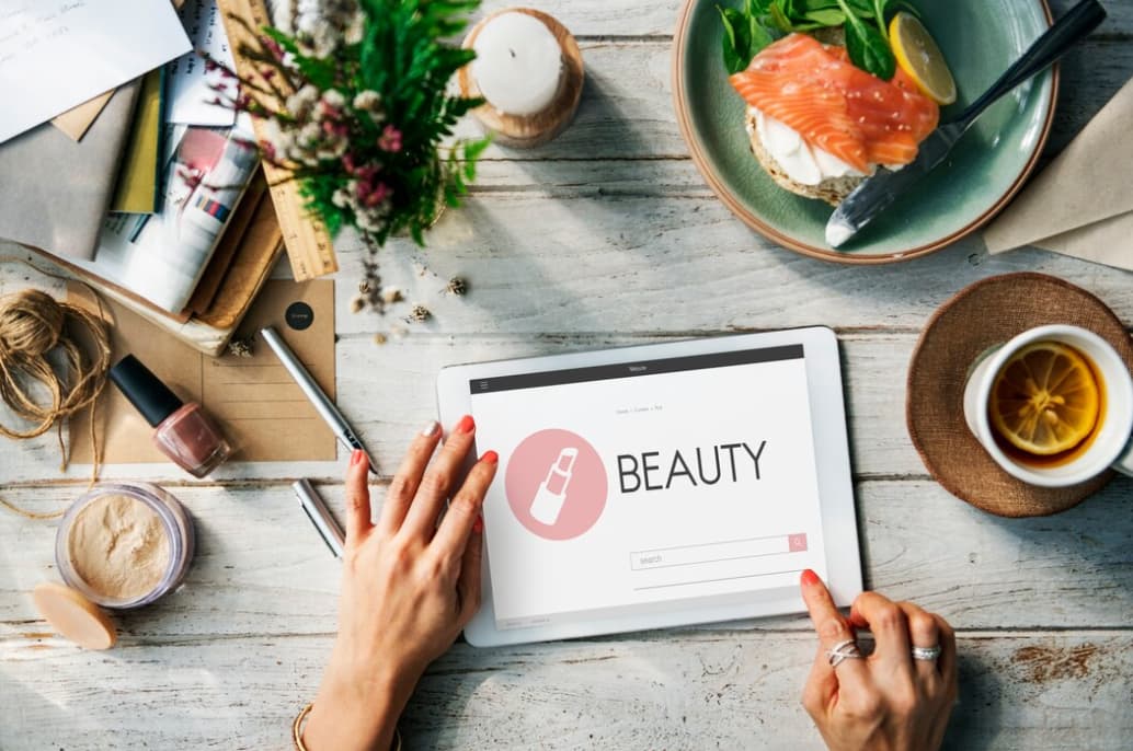 hands on the tablet with beauty website on it, cup of tee, and breakfast on the table