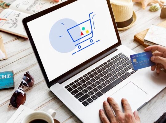 A person holding a credit card, shopping online with a laptop displaying a cart icon