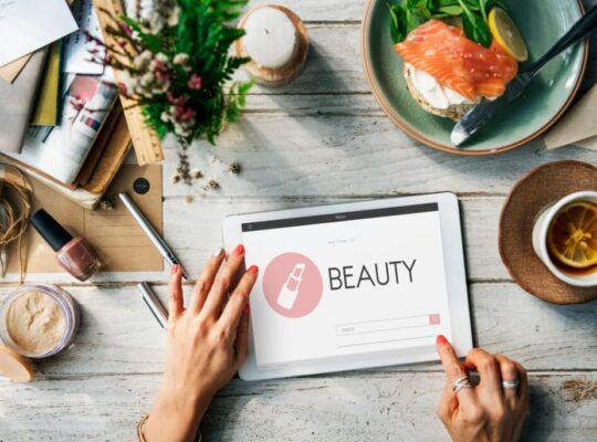 hands on the tablet with beauty website on it, cup of tee, and breakfast on the table